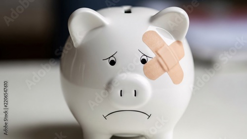 Sad white piggy bank with bandage on eye