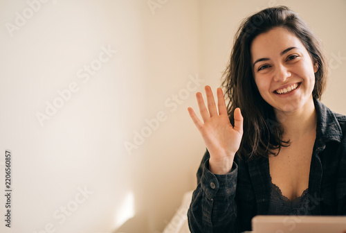 Young Caucasian woman waving hello at camera with friendly smile