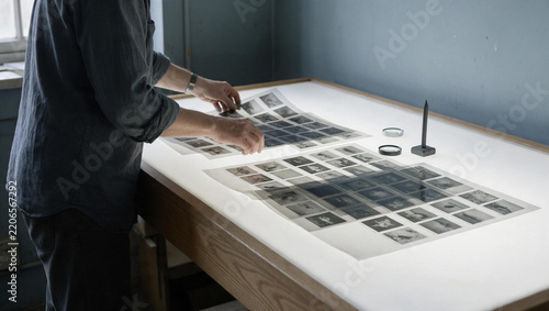 Archivist inspecting photographic film negatives on light table. Curating vintage photography contact sheets in laboratory