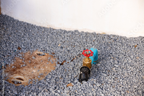 Colorful glass bottle lying on gray gravel beside white wall, viewed from above with scattered stones and earthy patch creating unusual outdoor scene