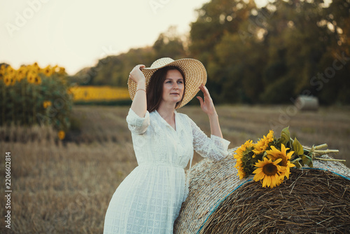 woman in a white dress holding a bouquet of wild flowers with sunflowers in a mowed field with straw bales