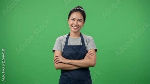 Confident young female entrepreneur smiling with crossed arms in navy apron over green background