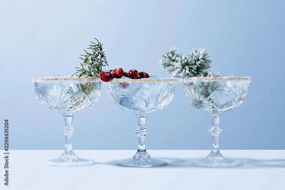 Obraz premium Three elegant coupe glasses with gilded rims and festive garnishes on a grey background, for party invitations and bar menus
