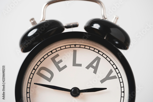 Delay concept with a close-up of a black vintage alarm clock displaying the word DELAY instead of numbers , it is symbolize missed deadlines, waiting time management and postponed plans schedule.