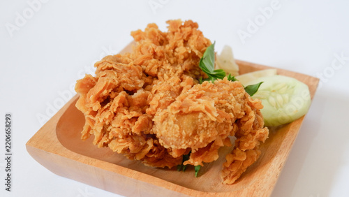 Crispy golden fried chicken wings served on a wooden plate with fresh cucumber slices and basil garnish, crunchy deep fried breaded poultry snack isolated on white background.