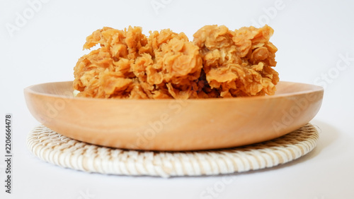 Delicious golden fried chicken with extra crispy breading served on a wooden plate against a white background. Gourmet crunchy deep-fried poultry snack for restaurant menus.