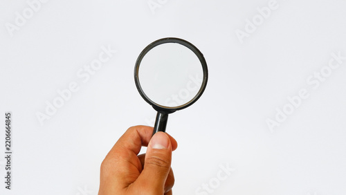 Person's hand holding a black magnifying glass isolated on white background, symbol of search, investigation, analysis, vision, and finding solutions in business or science.