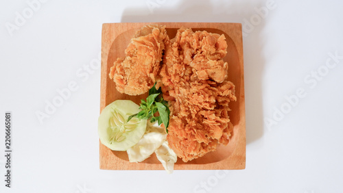 Crispy and delicious golden fried chicken pieces with a crunchy breaded texture, served on a wooden plate with fresh cucumber and cabbage garnish, isolated on white background.