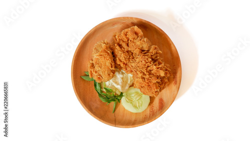 Crispy golden fried chicken served on a wooden plate with cucumber and basil garnish, isolated on white background. Top view of delicious deep fried poultry meat for menu.
