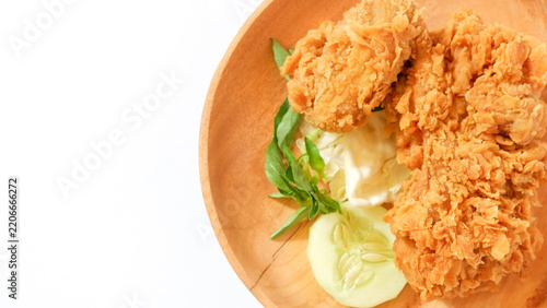 Crispy golden fried chicken served on a wooden plate with fresh cucumber, basil, and cabbage garnishes, isolated on a white background for food menu and restaurant marketing.