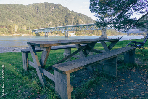Empty wooden picnic table on riverbank with mountain view