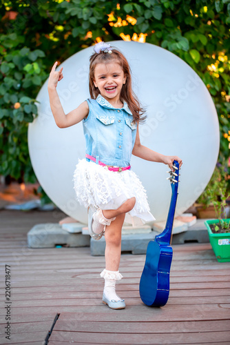 A little girl of European appearance plays the guitar on an impromptu stage, fantasizes that she is a musician. Children's games with imagination. Playing musical instruments.