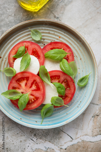 Italian caprese salad on a turquoise plate, vertical shot on a grey granite background, elevated view