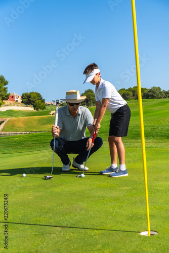 Instructor teaching boy putting golf lesson on green