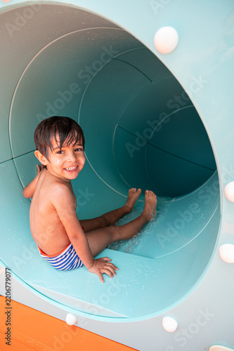 Obraz na plátně Cheerful young boy smiles while sliding down a bright blue water slide