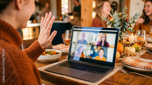 Woman waving hello during a video call on a laptop at a dinner party.