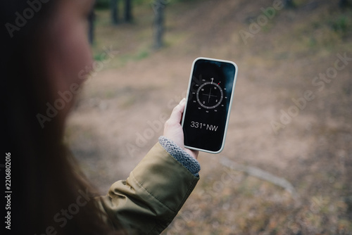 Woman using a smartphone compass while navigating through a forest trail, illustrating outdoor orientation, hiking technology, direction finding and nature exploration.