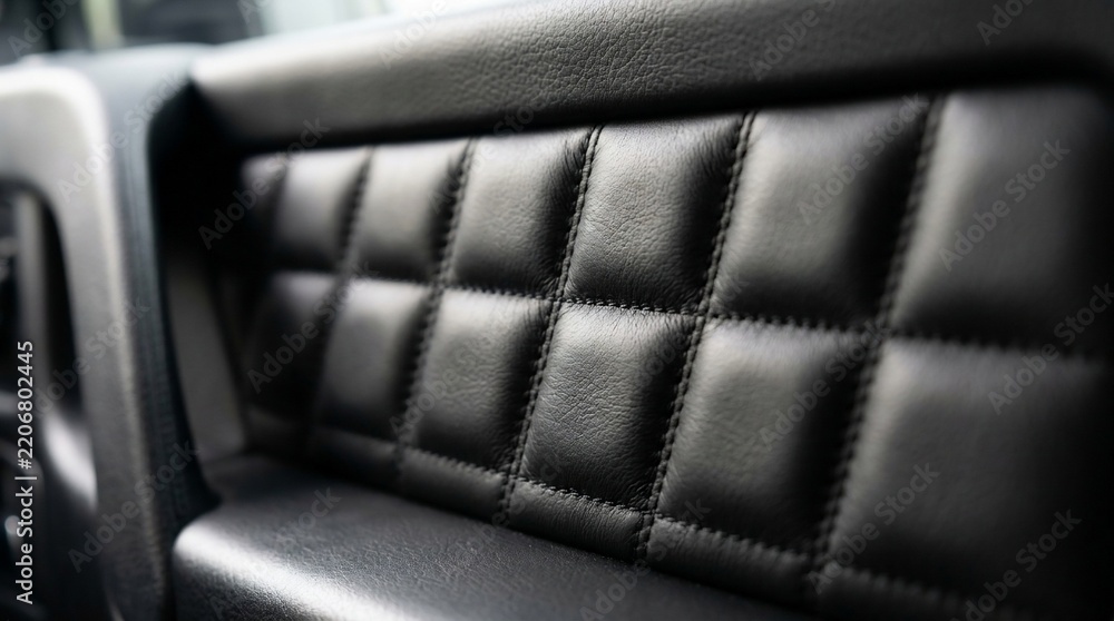 Naklejka premium Close-up of black quilted synthetic leather upholstery on a car door interior panel with elegant stitching and luxury textured details.