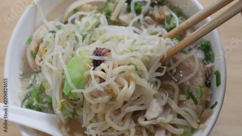Chopsticks lifting noodles and bean sprouts from ramen