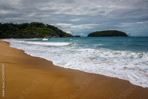 Tropical secluded beach with golden sand, scenic green hill and ocean waves under blue sky