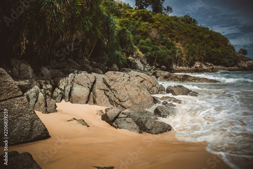 Tropical secluded beach with golden sand, scenic green hill and ocean waves under blue sky
