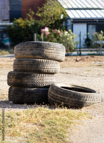 A stack of four old, weathered black car tires resting on dry ground, with another tire lying flat beside them against a blurred rural background.
