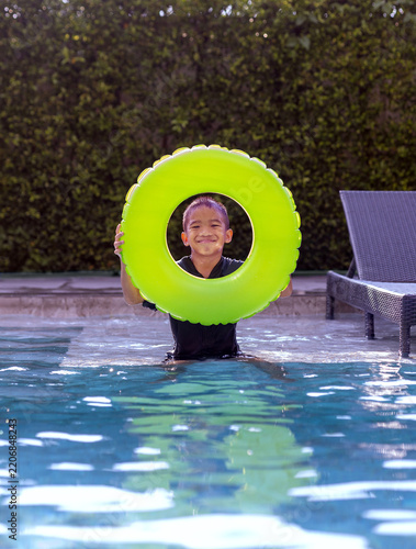 Cute Asian Boy Looking Through a Bright Green Inflatable Swim Ring in Pool