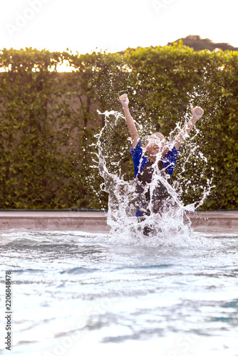 Joyful Boy Raising Arms in Celebration While Splashing Water in Pool