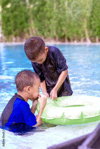 Asian Brothers Playing and Trying to Blow Up a Green Inflatable Swim Ring in a Swimming Pool on a Summer Vacation Day