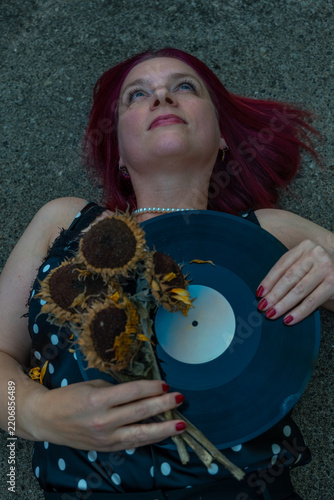 Woman lies on ground holding vinyl record and dried sunflowers in an urban setting