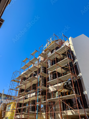 Construction of a building with scaffolding under a clear blue sky in an urban area