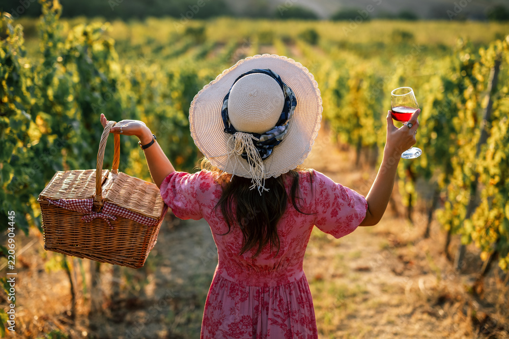 Obraz premium Back view of woman celebrating summer evening with wine glass in vineyard