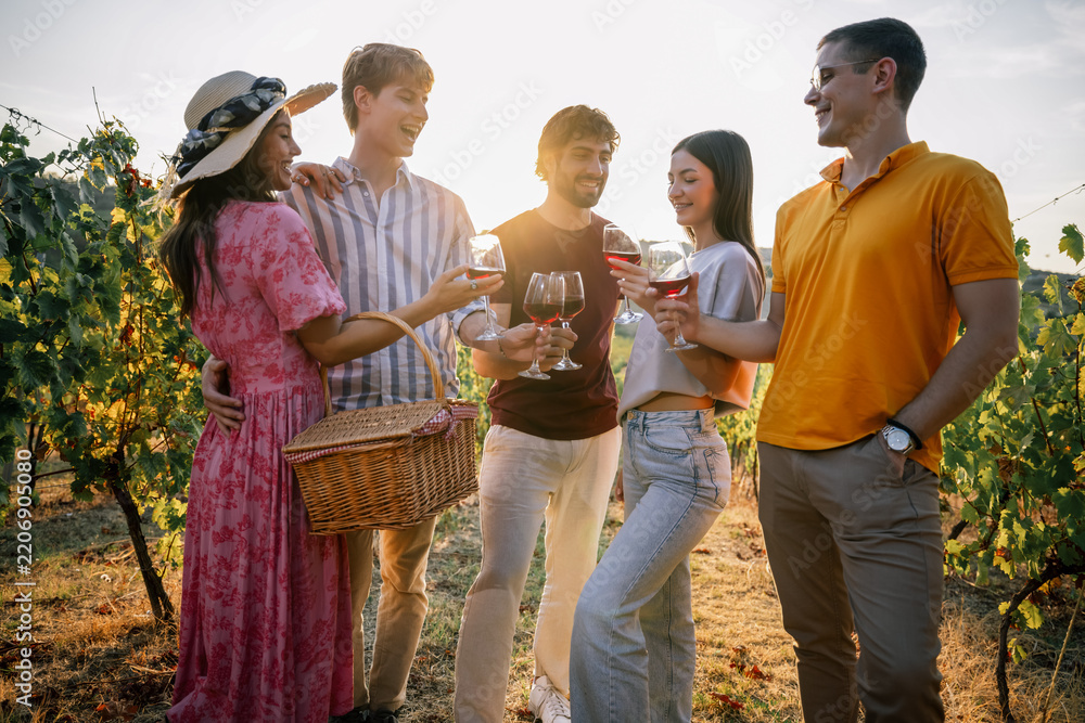 Obraz premium Group of young friends toasting with glasses of red wine in vineyard