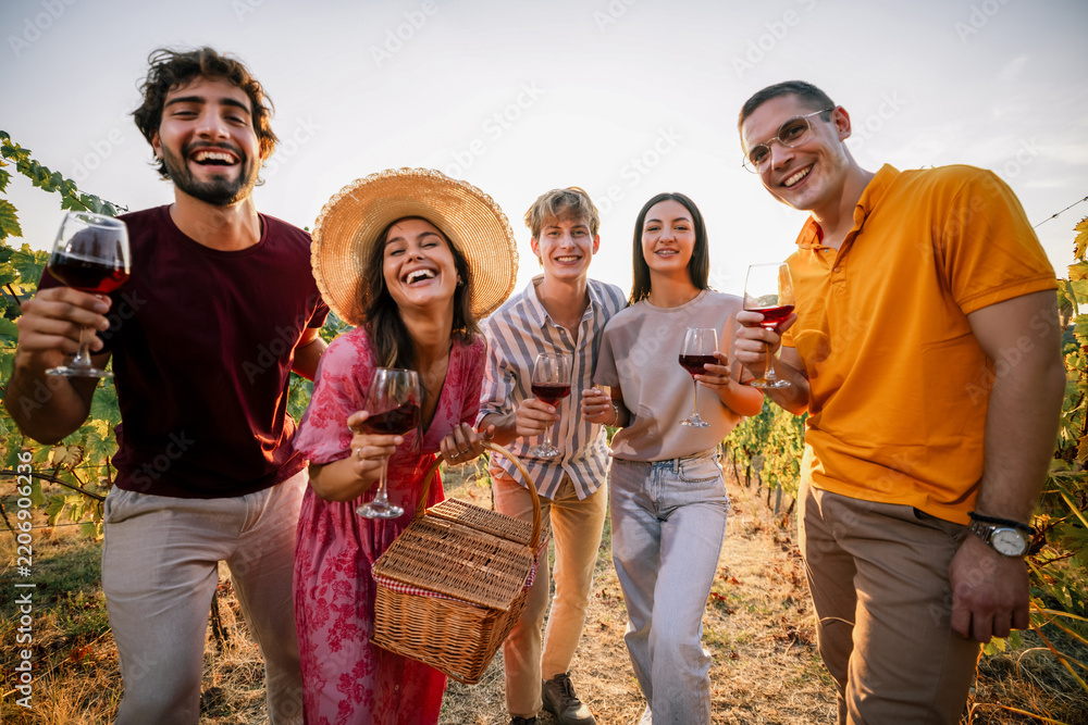 Obraz premium Group of smiling friends posing closely with red wine in sunset vineyard