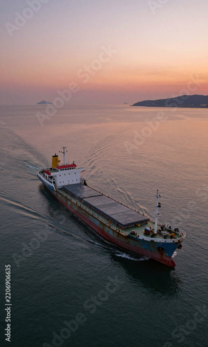 aerial photograph taken high angle calm bay golden hour weathered small cargo ship motion amidst vibrant orange