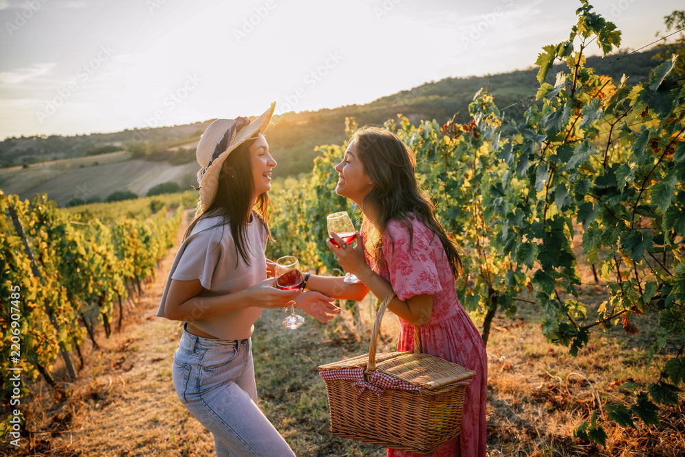 Obraz premium Two female friends laughing and holding wine glasses in a vineyard