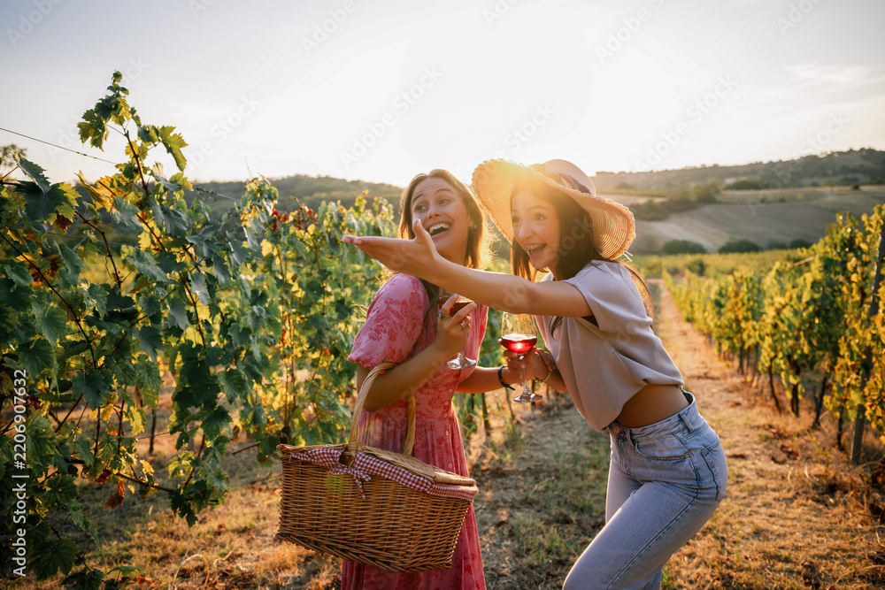 Obraz premium Two happy women pointing and laughing during vineyard wine tasting