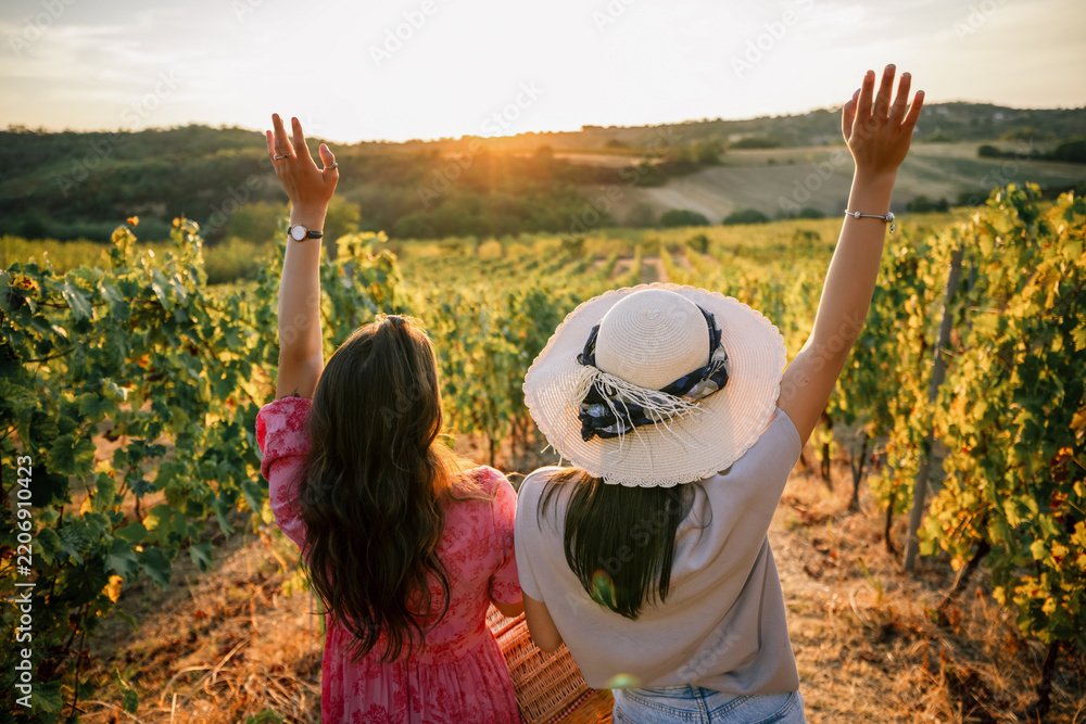 Obraz premium Two female friends raising hands in joy at vineyard sunset