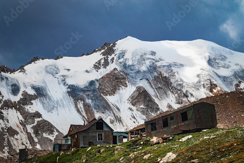 Old wooden huts of the T1 research station at the foot of Molodezhny Glacier. High altitude scientific base in Almaty mountains. Dramatic alpine scenery with snow and ice.