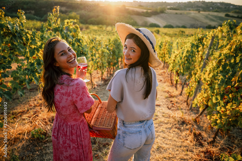Obraz premium Two smiling female friends looking back over shoulder in vineyard