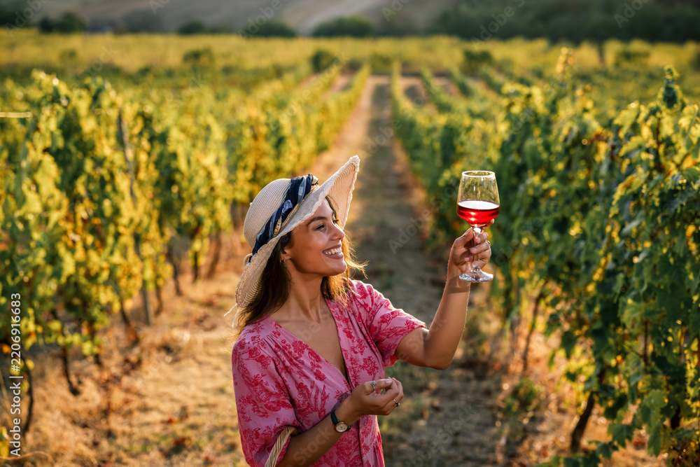 Obraz premium Woman holding up glass of red wine evaluating quality in vineyard