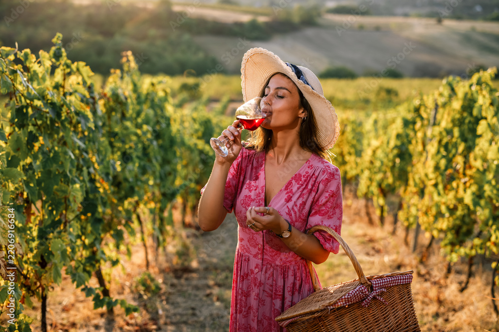 Obraz premium Woman drinking glass of red wine in sunny vineyard field