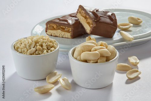 Layered chocolate candy bar with caramel and peanuts broken in half with nut bowls