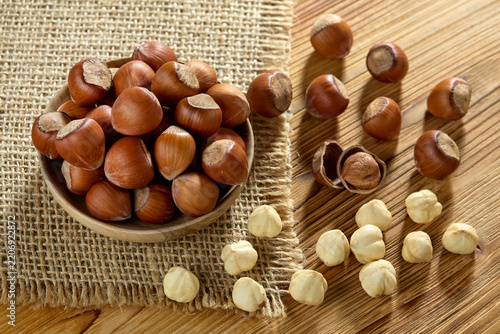 Raw whole hazelnuts in shell in a wooden bowl with peeled nuts on a rustic wooden table