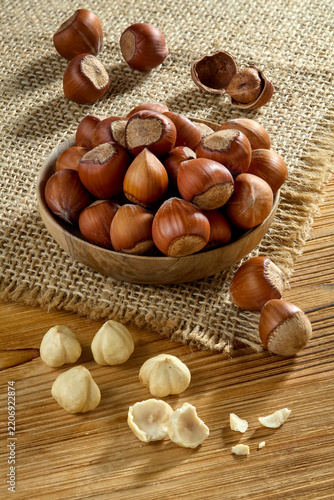 Raw whole hazelnuts in shell in a wooden bowl with peeled nuts on a rustic wooden table
