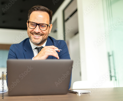 Professional businessman smiling while working on a laptop, engaging with legal documents or financial data, representing success, productivity, and an efficient corporate workflow
