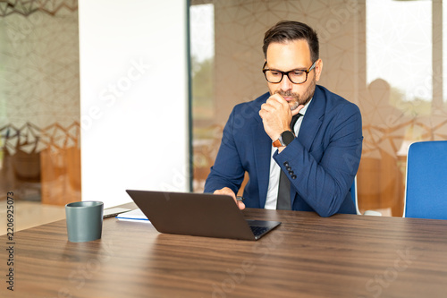 Professional businessman analyzing information on a computer, sitting at a desk and contemplating business decisions, legal advice, and accounting tasks in a corporate setting
