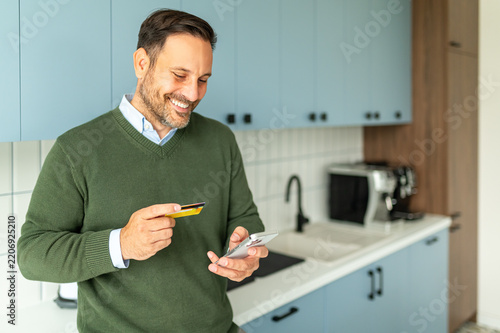 Man smiling while confidently holding a credit card and mobile phone, engaging in convenient online shopping and secure digital financial transactions