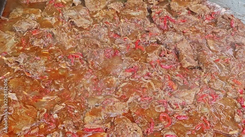 a large batch of a braised or stewed meat dish, resembling a beef stew or goulash cooked with sliced red peppers and onions in a rich, reddish-brown gravy.