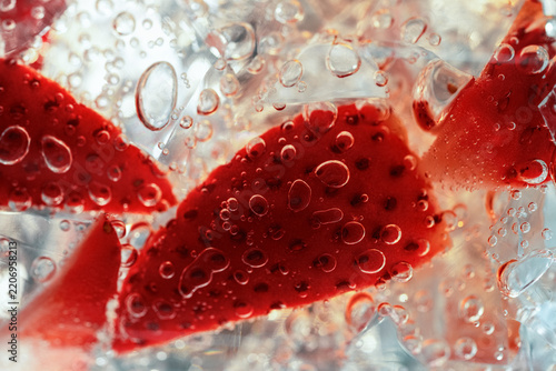 Macro view of fresh strawberry slices with crystal ice and sparkling bubbles. Vibrant summer refreshment background with vivid red fruit